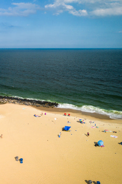 A sunny beach scene with golden sand, scattered beachgoers under colorful umbrellas, and gentle waves from a calm ocean meeting the shoreline.