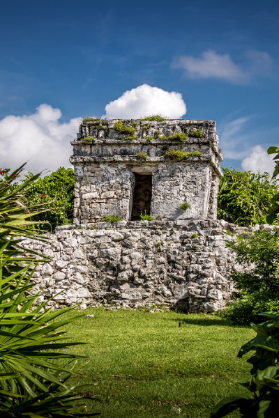 Ancient stone structure surrounded by lush greenery under a bright blue sky with scattered clouds.