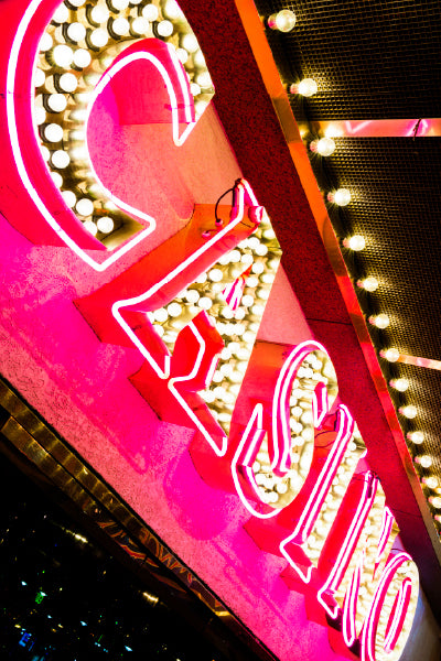 A bright, neon-lit "CASINO" sign glowing in pink and white, mounted on a building exterior with multiple light bulbs surrounding it, creating a vibrant and flashy atmosphere.