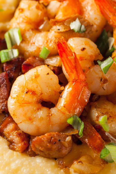 Close-up of a dish featuring cooked shrimp, pieces of meat, and chopped green onions served over creamy grits.
