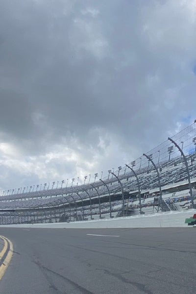 Empty race track with high safety fencing and grandstands under a cloudy sky, capturing the calm before or after an event at a major speedway.